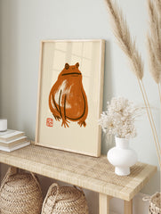 Minimalist brown frog ink-wash illustration with a small red seal on a beige background, in an alternate framed mockup
