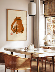 Minimalist brown frog ink-wash illustration with a small red seal on a beige background, in a styled room mockup