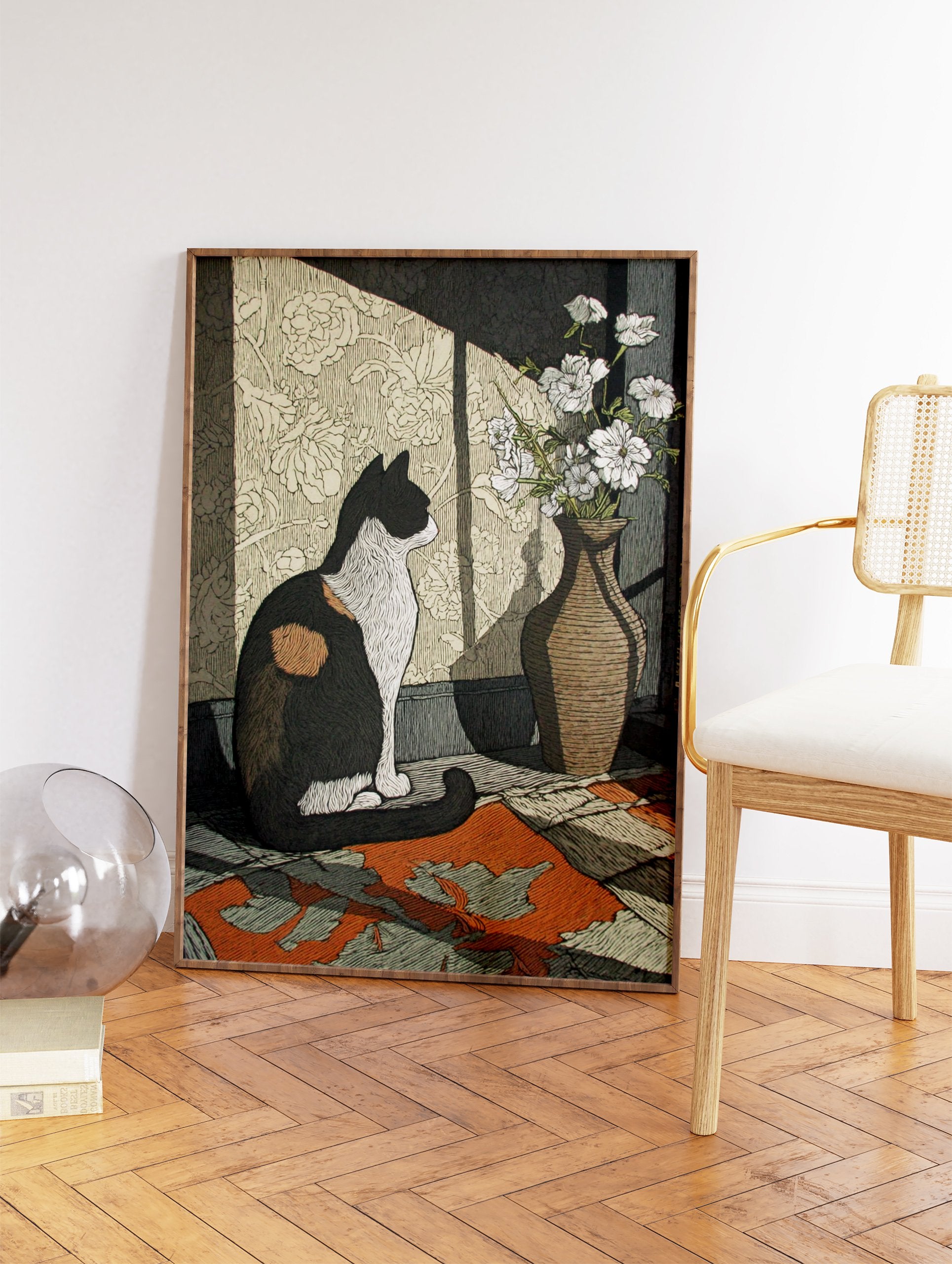 Illustrative calico cat wall art print sitting next to a vase of white flowers, with sunlight casting shadows on patterned wallpaper. - Image 2