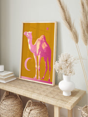 Pink camel, crescent moon, and star on a mustard yellow background, in a bold illustrative, in an alternate framed mockup