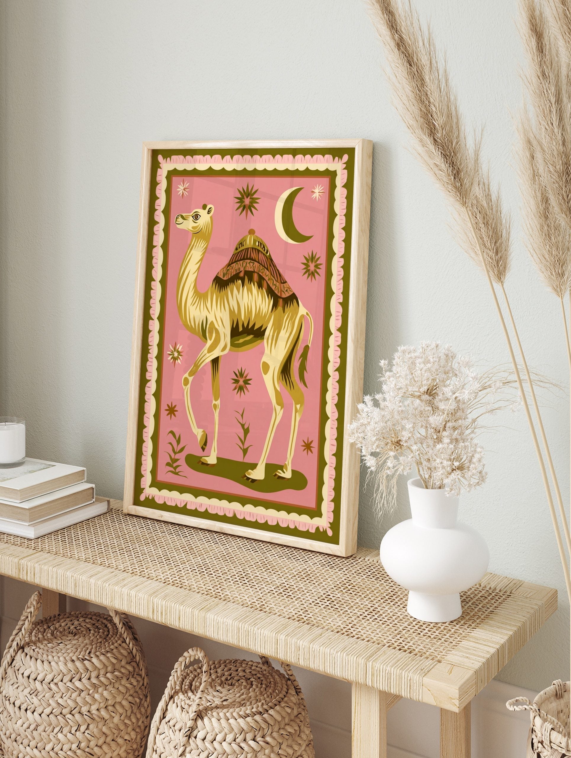 Illustrative camel with ornate saddle, crescent moon, and stars on pink background with green, in an alternate framed mockup