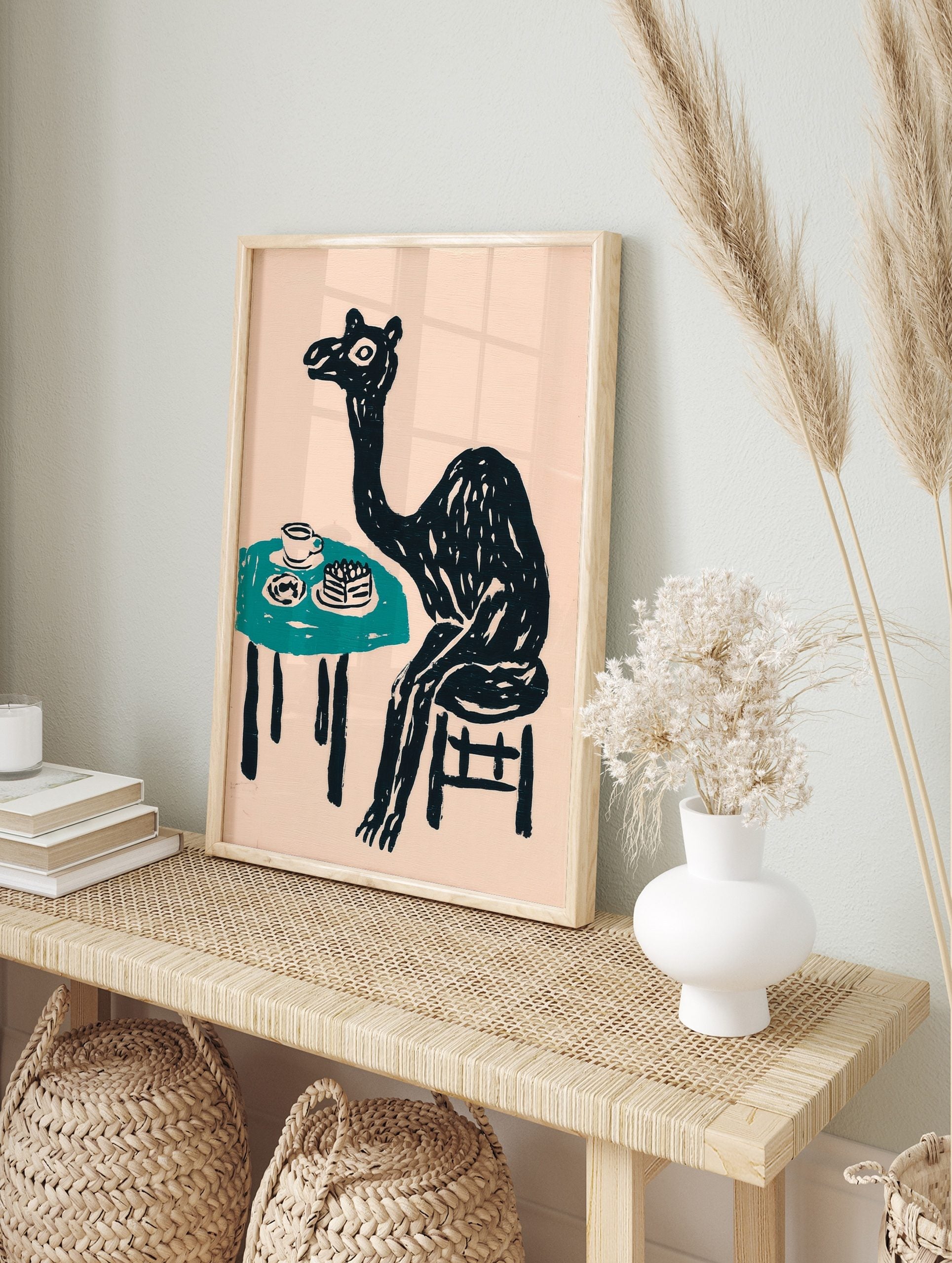 Whimsical black camel sitting at a teal table with cake and a cup, against a pale pink, in an alternate framed mockup