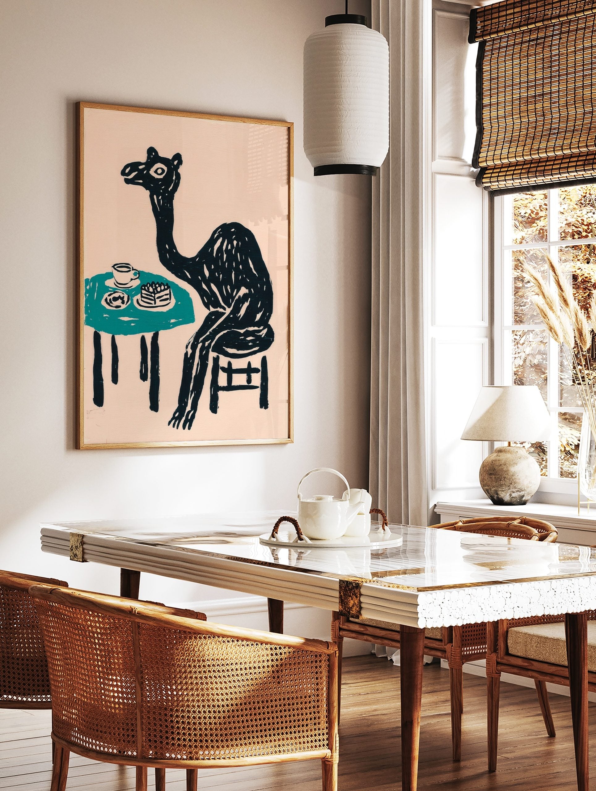 Whimsical black camel sitting at a teal table with cake and a cup, against a pale pink background, in a styled room mockup