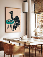 Whimsical black camel sitting at a teal table with cake and a cup, against a pale pink background, in a styled room mockup