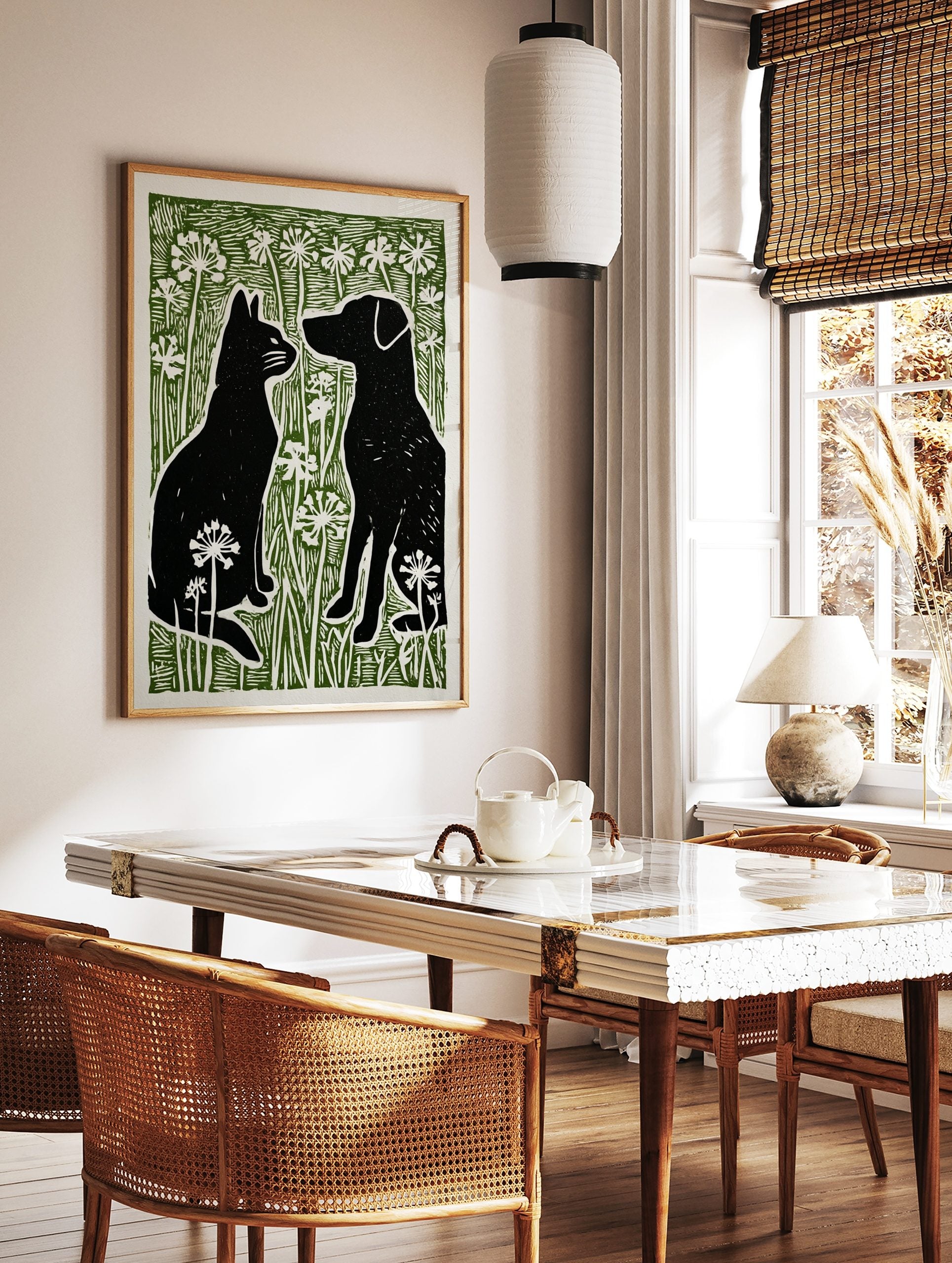 Black cat and dog silhouettes facing each other in green grass with white flowers, linocut style, in a styled room mockup