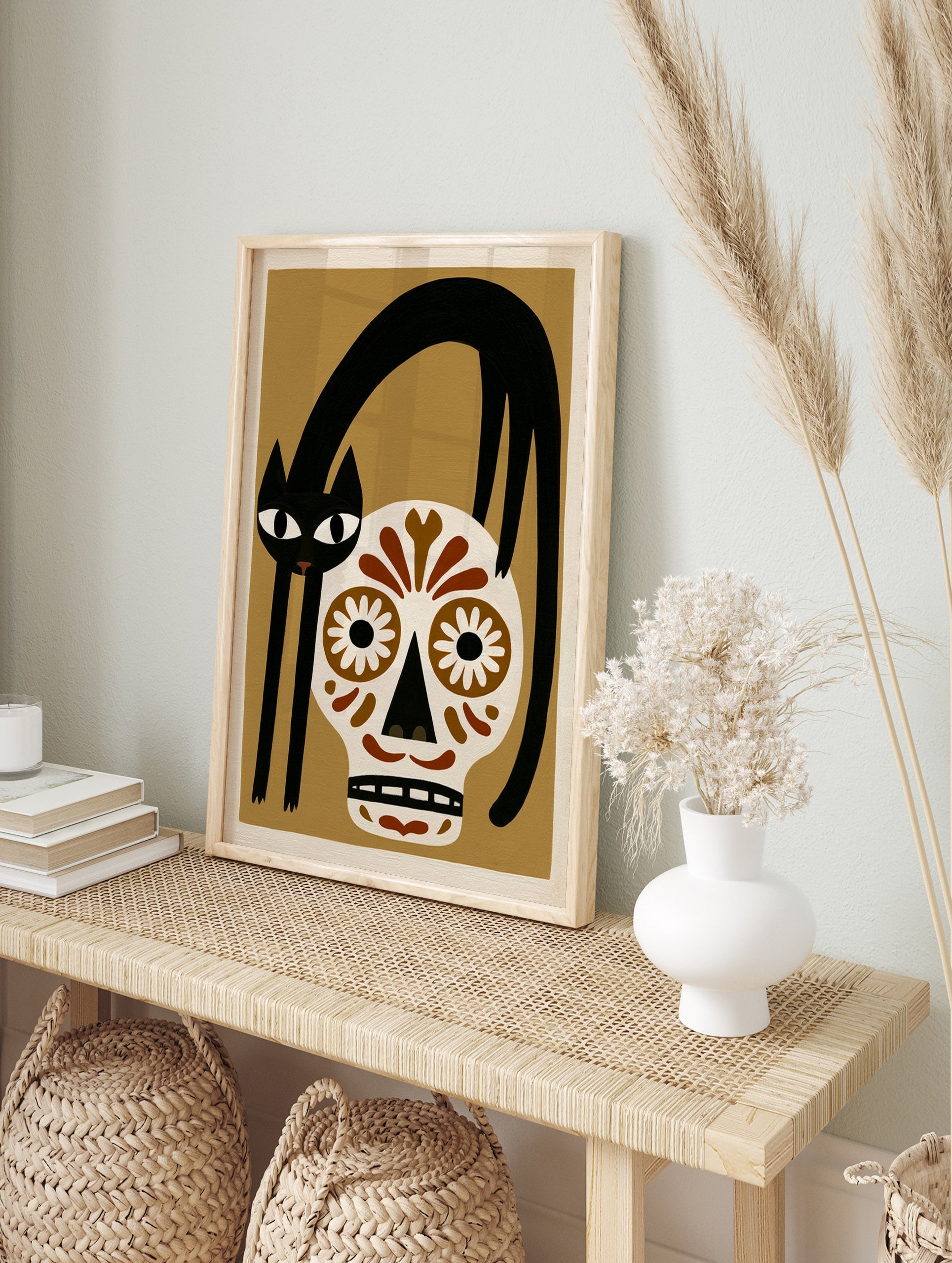 Illustrative wall art of a black cat arched over a brown and white sugar skull on a tan, in an alternate framed mockup