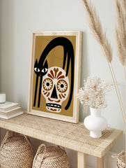 Illustrative wall art of a black cat arched over a brown and white sugar skull on a tan, in an alternate framed mockup