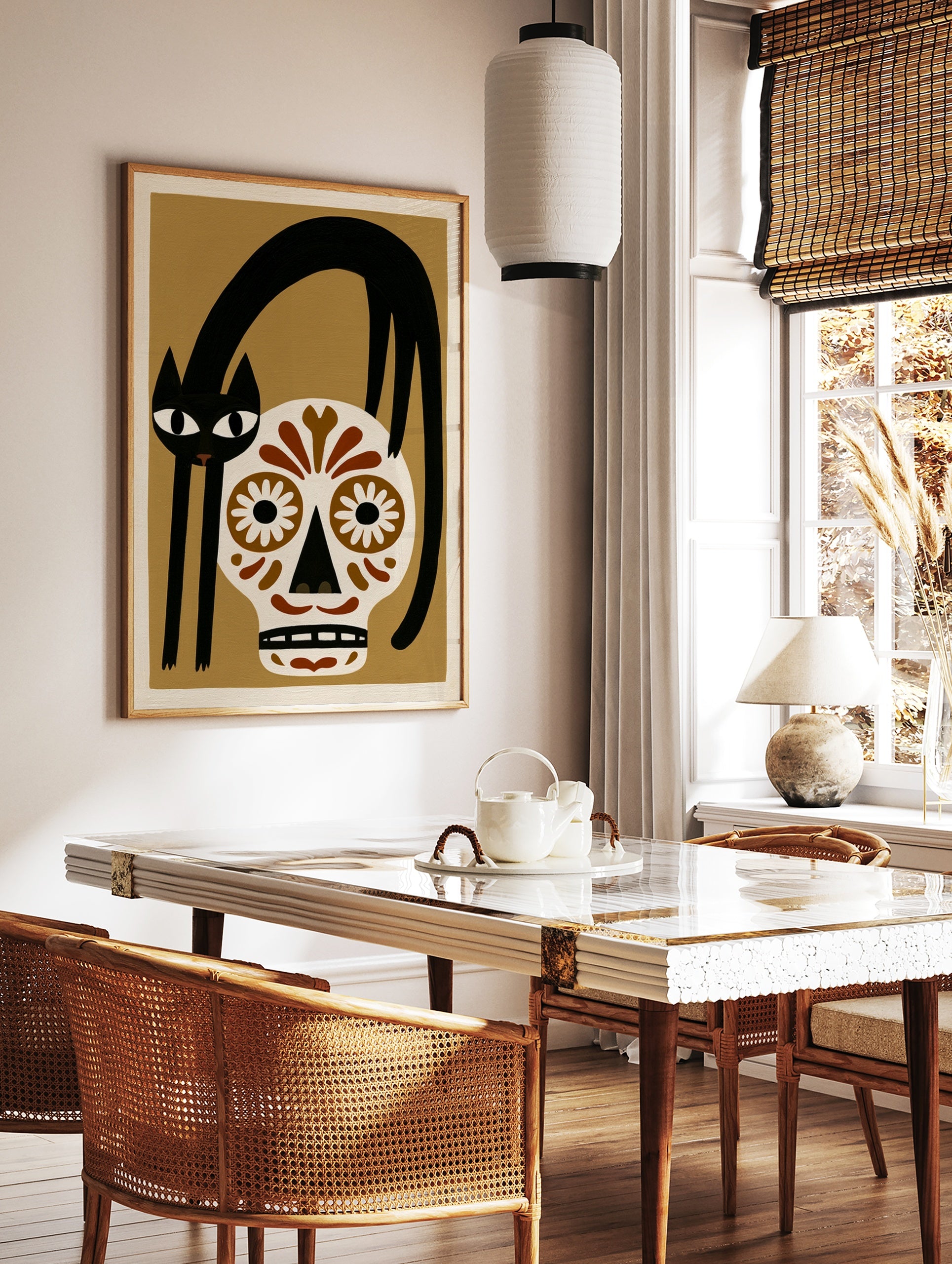 Illustrative wall art of a black cat arched over a brown and white sugar skull on a tan background, in a styled room mockup