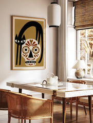 Illustrative wall art of a black cat arched over a brown and white sugar skull on a tan background, in a styled room mockup