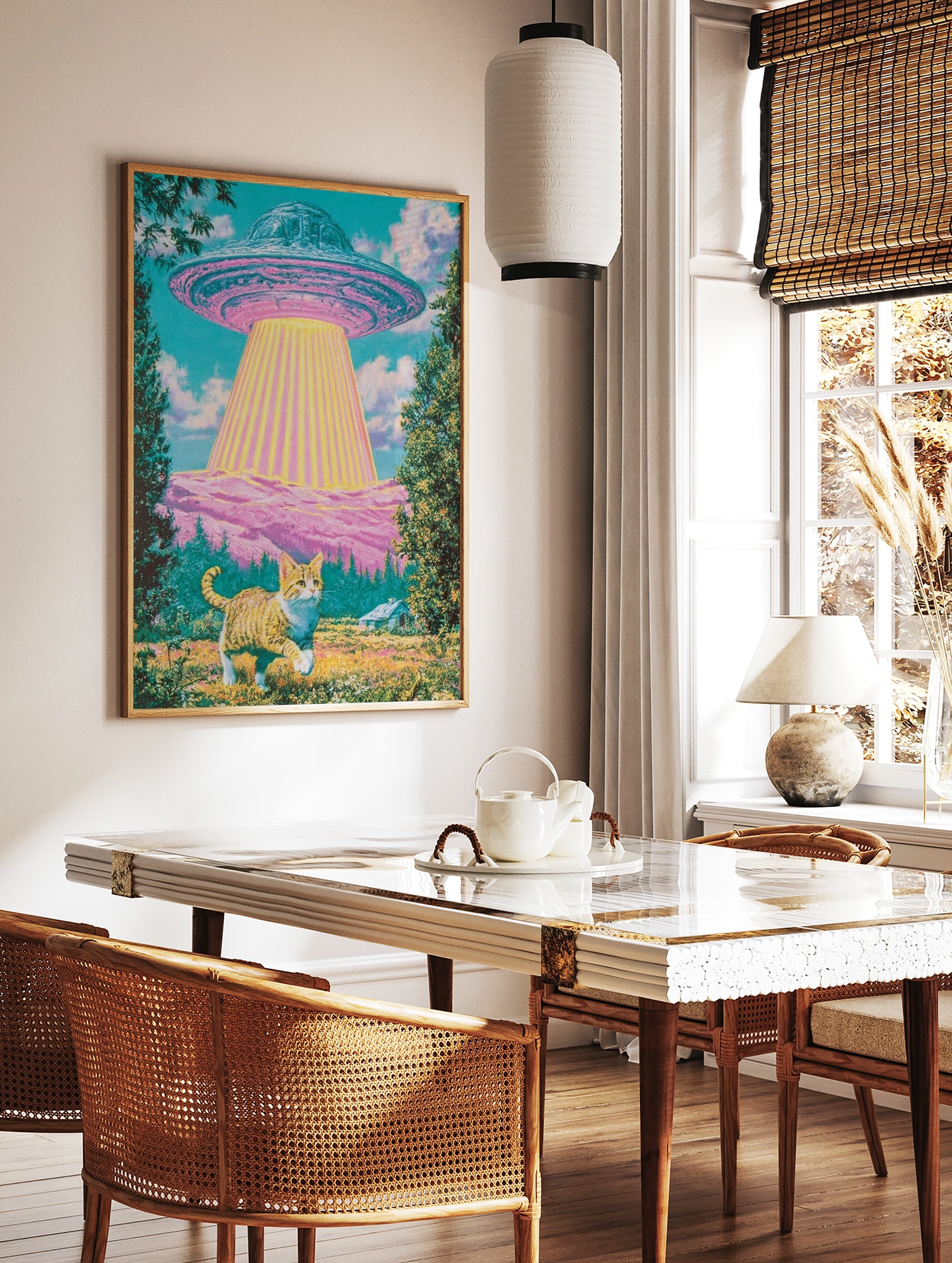 Surreal art print of a ginger cat standing in a meadow looking up at a glowing UFO above pink hills, in a styled room mockup