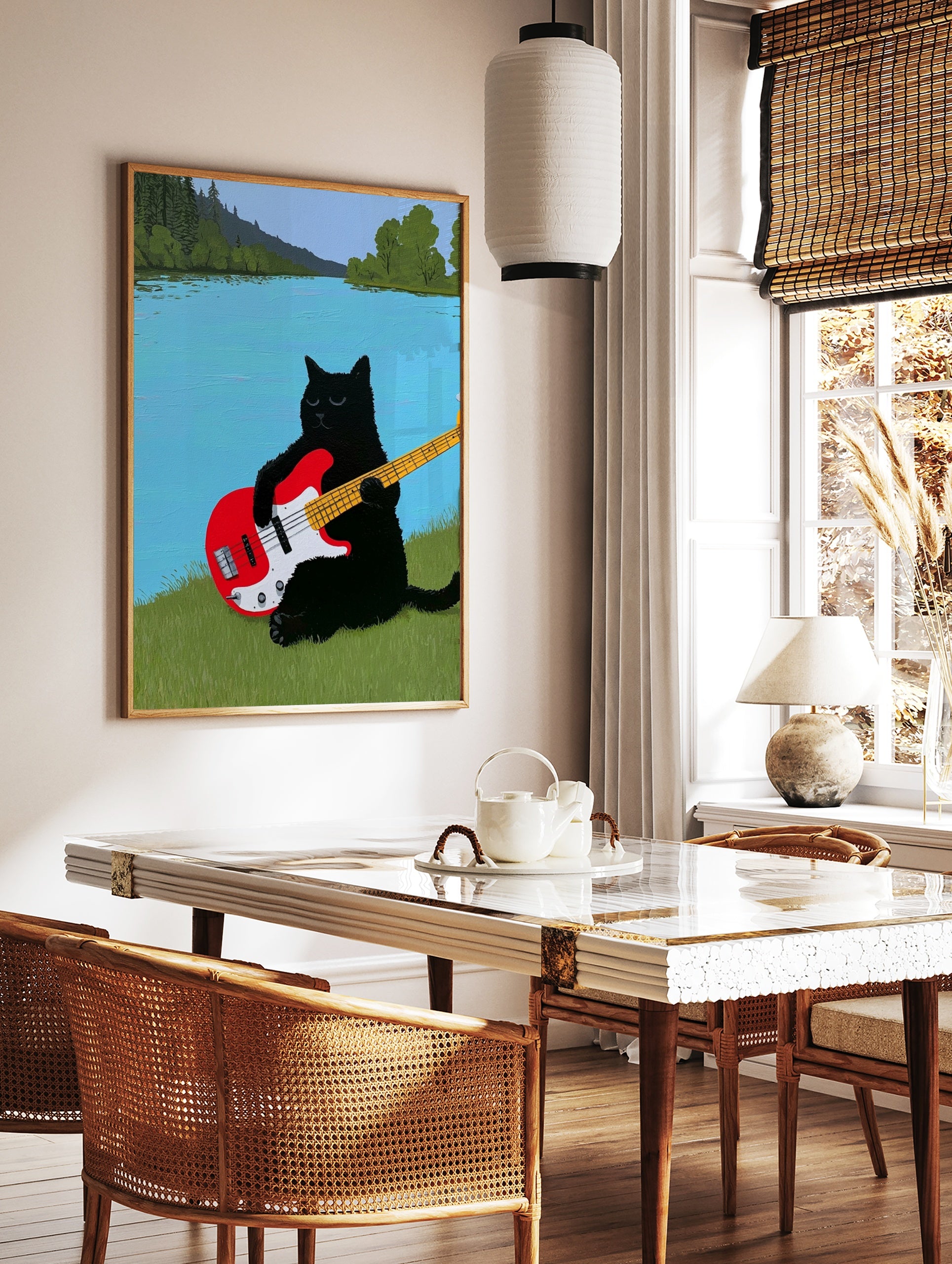 Black cat playing a red electric bass guitar on a grassy riverbank with a blue river and trees, in a styled room mockup