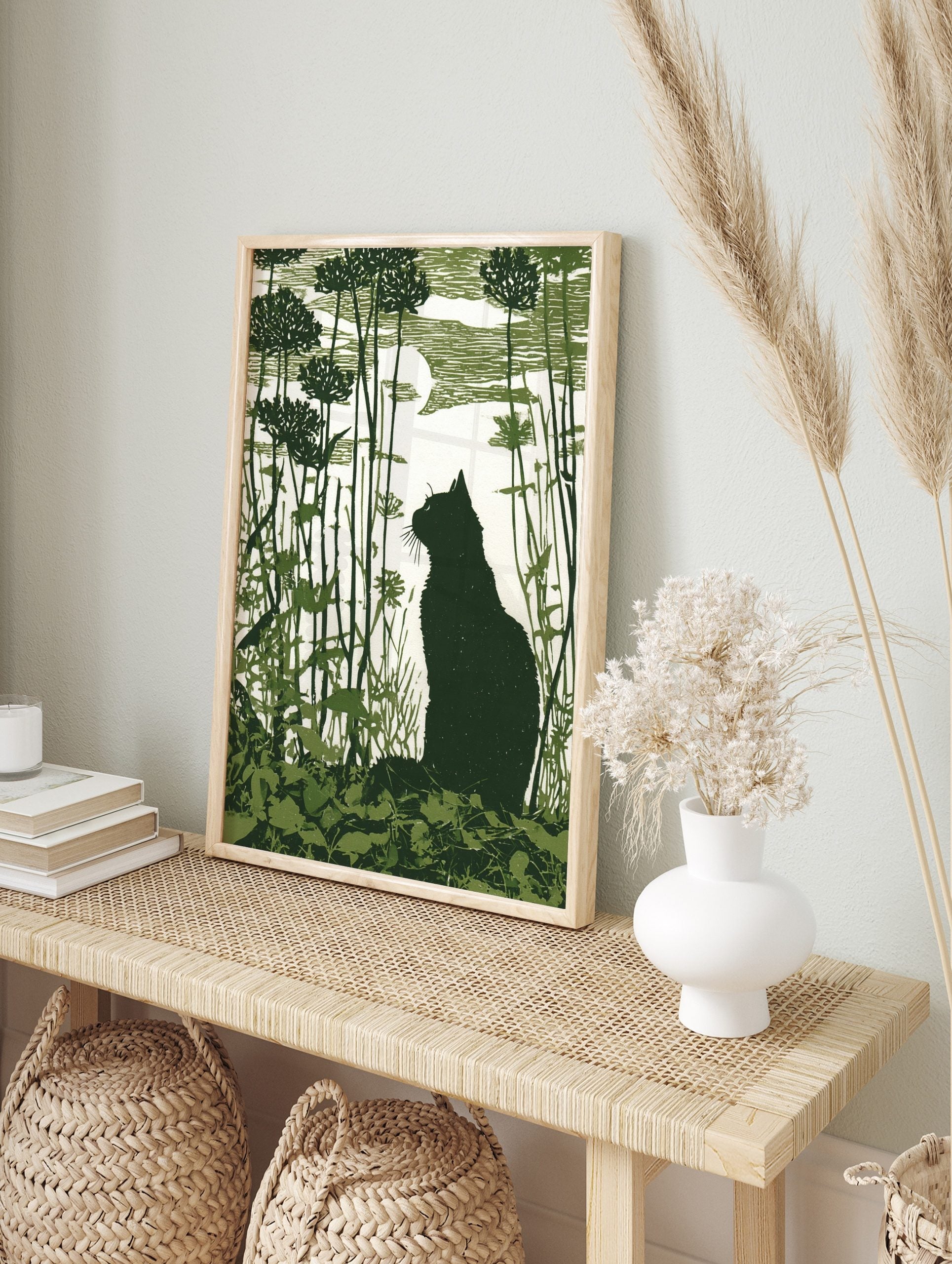Dark green linocut-style print of a cat silhouette in a garden with tall plants and a moon, in an alternate framed mockup