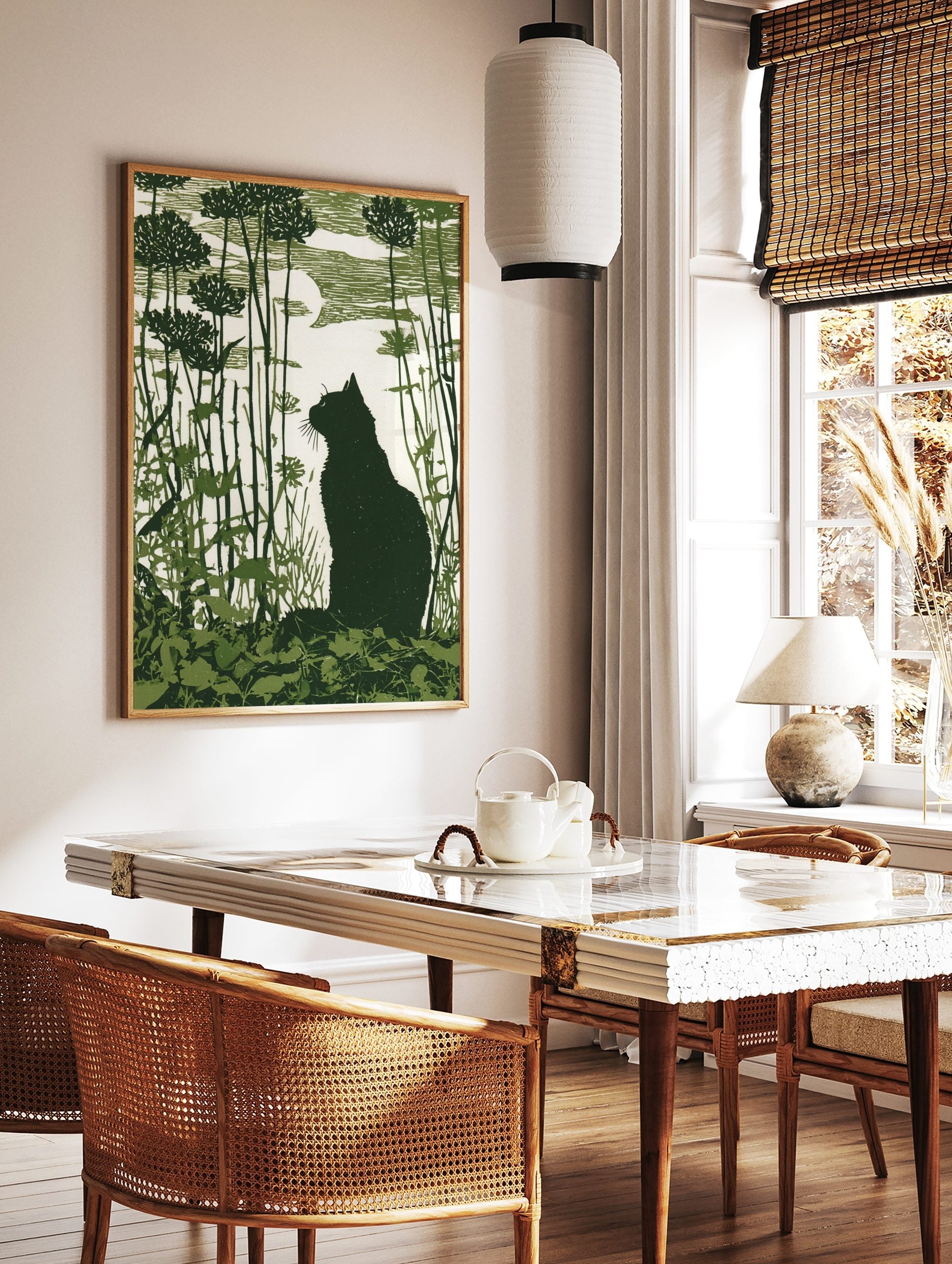 Dark green linocut-style print of a cat silhouette in a garden with tall plants and a moon, in a styled room mockup