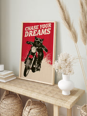 Black cat wearing motorcycle goggles on a bike with red background and the text Chase Your, in an alternate framed mockup