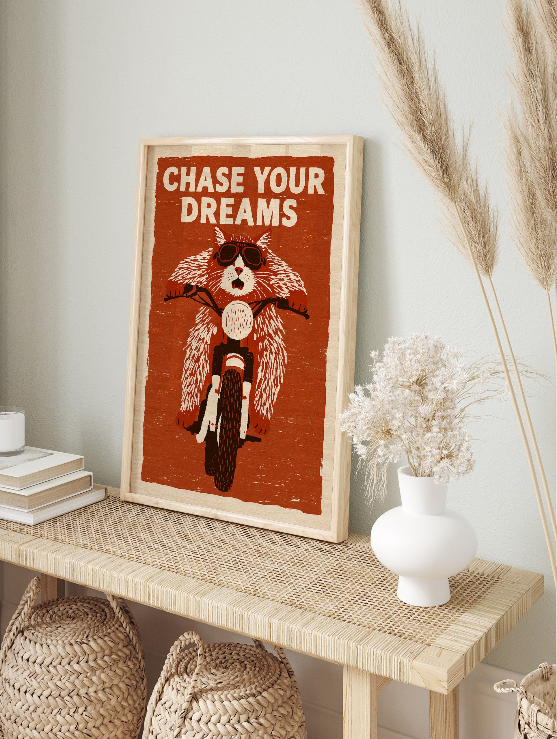 Illustration of a cat wearing goggles on a motorcycle with the text Chase Your Dreams on a, in an alternate framed mockup