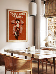 Illustration of a cat wearing goggles on a motorcycle with the text Chase Your Dreams on a textured, in a styled room mockup