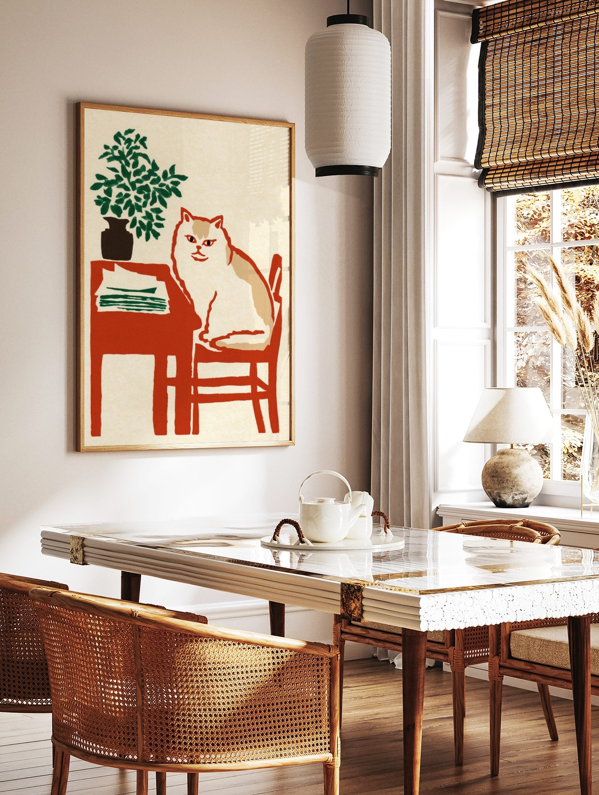 Illustrative print of a white and tan cat on a red chair next to a table with a green plant and, in a styled room mockup