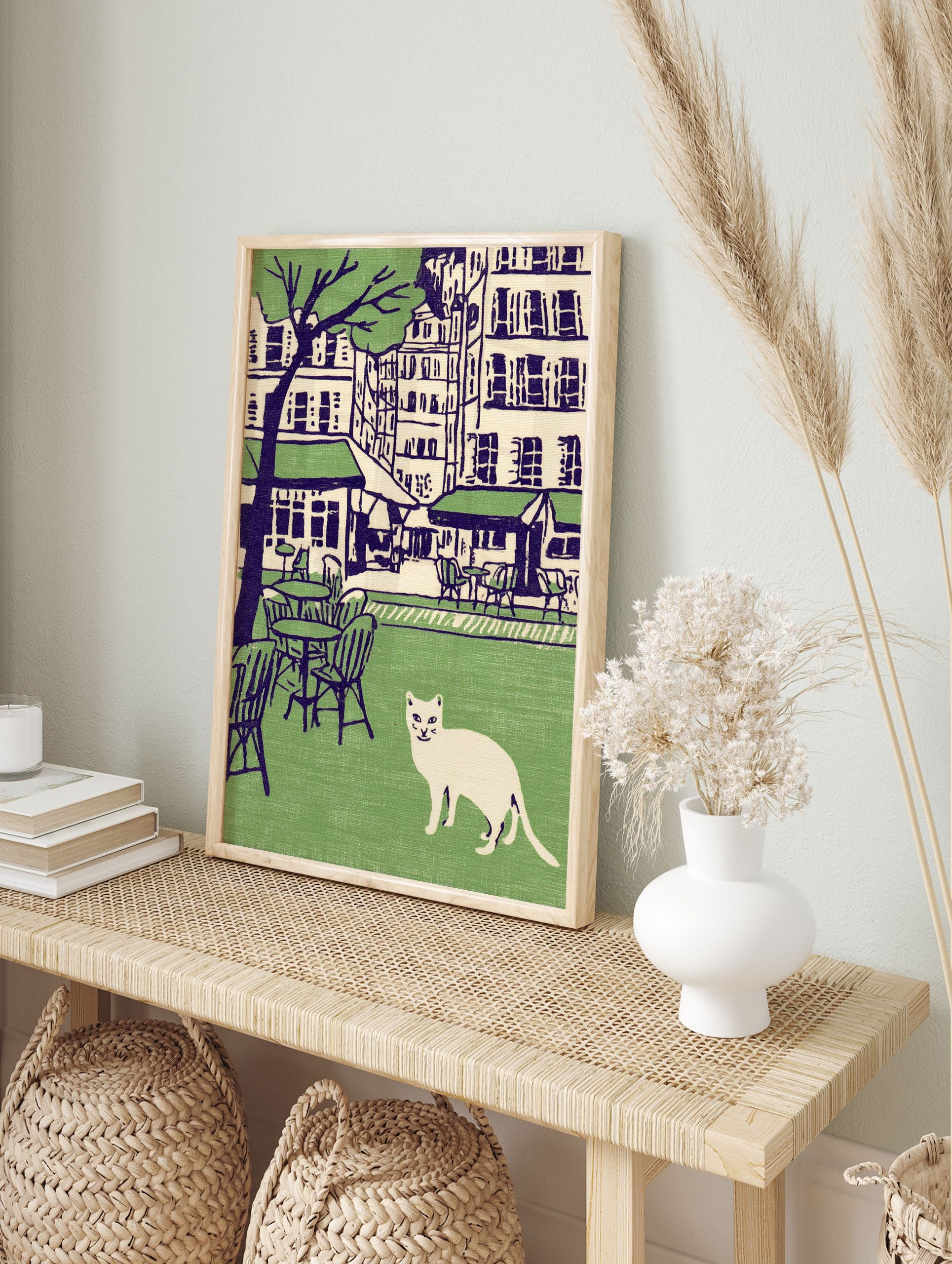 Illustration of a white cat in a green park with cafe tables, chairs, city buildings, and a tree in the background. Cat wall art. - Image 3