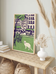 Illustration of a white cat in a green park with cafe tables, chairs, city buildings, and a tree in the background. Cat wall art. - Image 3