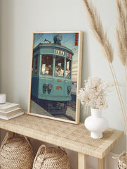Illustrative print of numerous cats riding a teal-blue Japanese tram with visible Japanese, in an alternate framed mockup