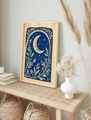 Illustrative deep blue botanical print with a cream crescent moon, stars, and leafy branches, in an alternate framed mockup