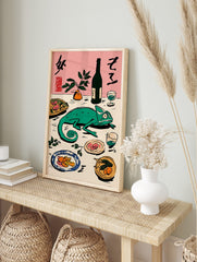 Green chameleon on a table with Japanese calligraphy, bottle, plant, and plates of food on a, in an alternate framed mockup