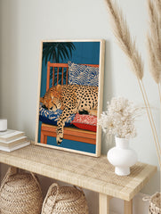 Illustration of a sleeping cheetah on a wooden bench with patterned cushions and palm leaves, in an alternate framed mockup