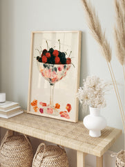 Illustrative wall art of red and dark cherries in a stemmed glass bowl on a neutral background, in an alternate framed mockup