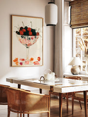 Illustrative wall art of red and dark cherries in a stemmed glass bowl on a neutral background, in a styled room mockup