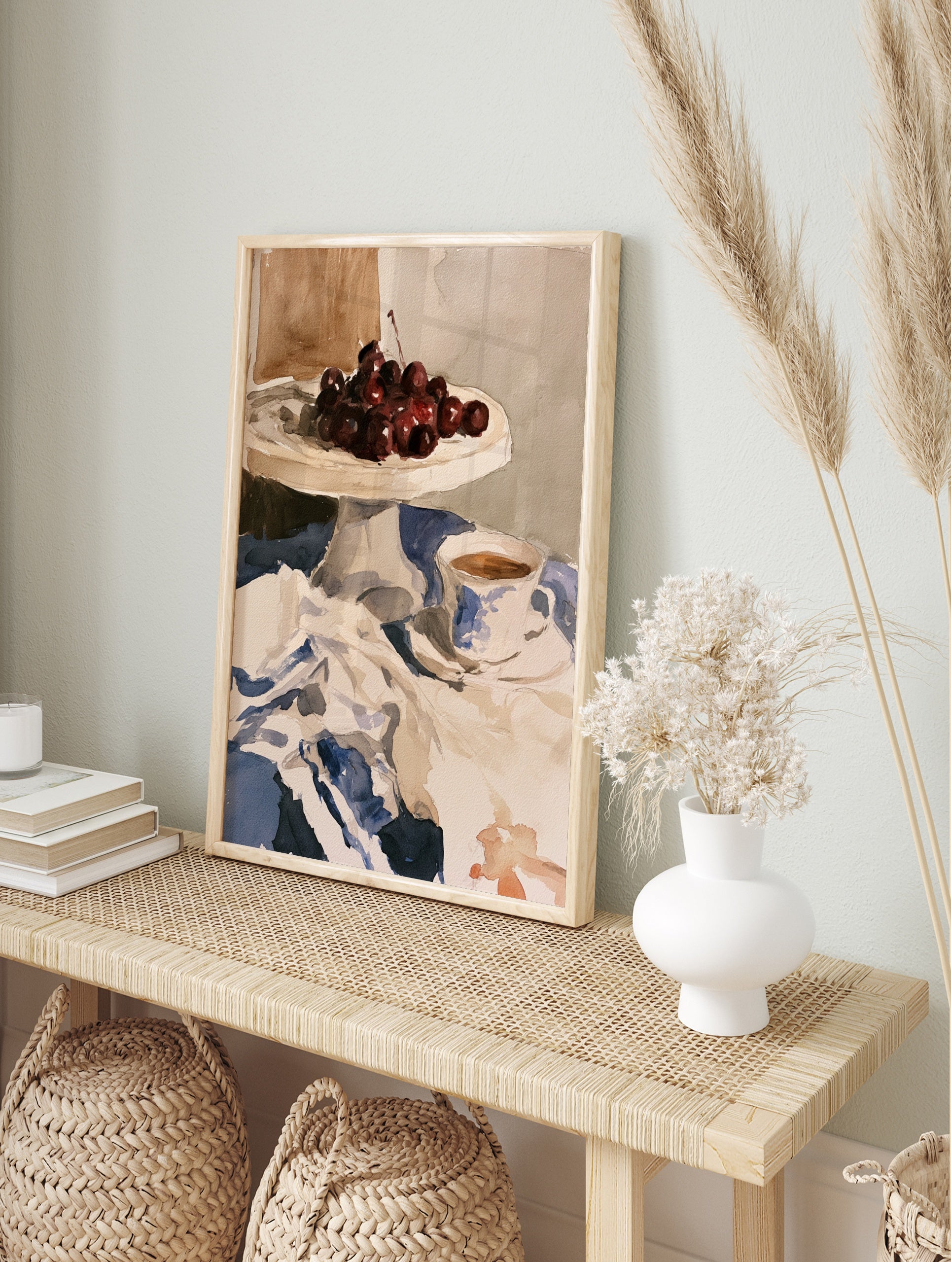 Watercolour still life print of cherries on a cake stand and a teacup on a blue tablecloth, in an alternate framed mockup