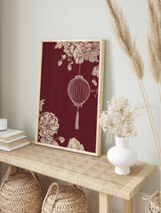 Illustrative Chinese lantern with tassel, cream botanical flowers, and foliage on a maroon, in an alternate framed mockup