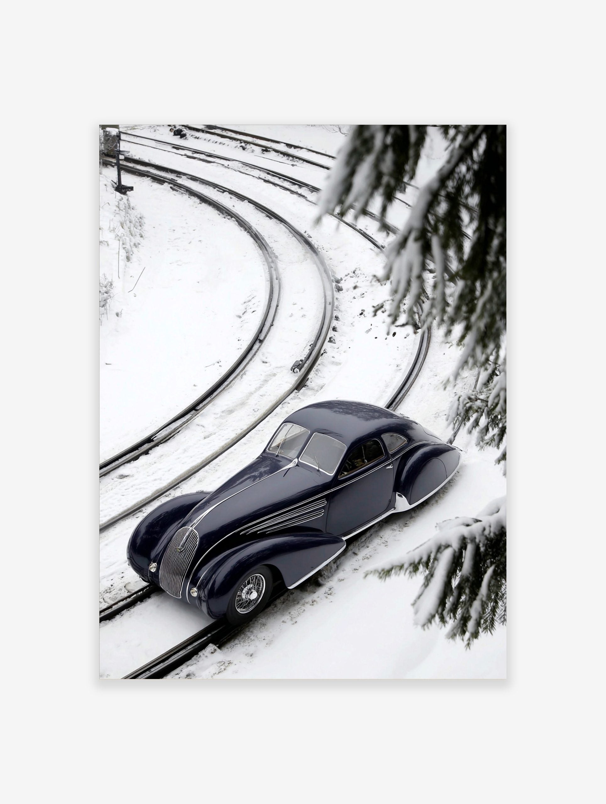 Navy blue classic car on snow-covered train tracks, high-angle view with pine branches and curving rails