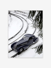 Navy blue classic car on snow-covered train tracks, high-angle view with pine branches and curving rails