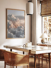 Aerial view of fluffy white and grey clouds with soft peachy light across a vast sky, in a styled room mockup