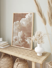 Warm sepia-toned photographic print of large, layered cumulus clouds against a soft sky, in an alternate framed mockup