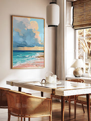 Colourful painterly beach scene art print with blue and peach clouds, turquoise ocean, and pink sand, in a styled room mockup