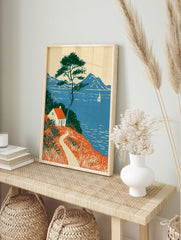 Coastal cottage wall art with red roof house, pine tree, and sailboat on blue sea landscape, in an alternate framed mockup