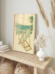 Illustrative print of green and white striped deckchair on balcony overlooking blue sea and, in an alternate framed mockup