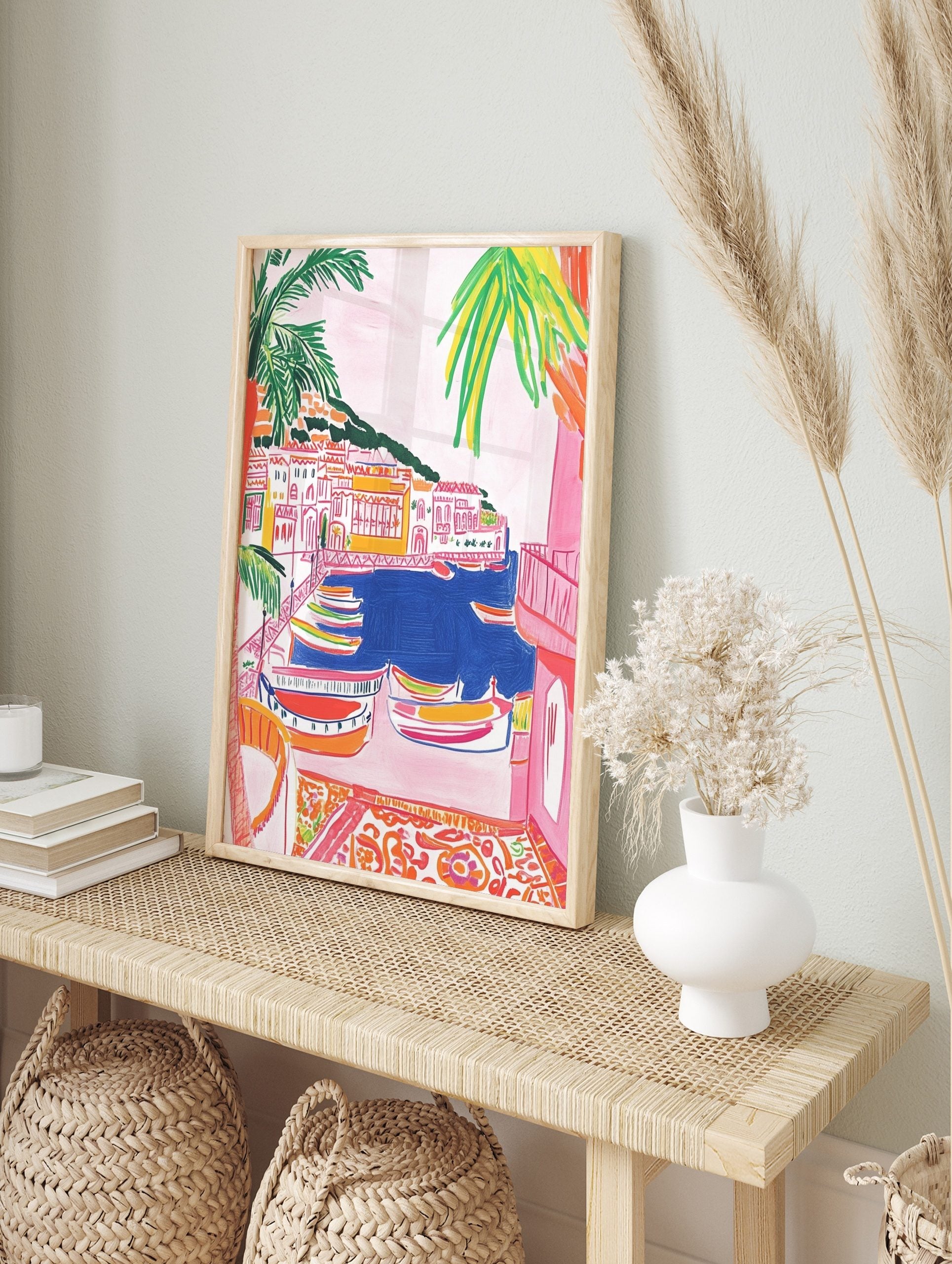 Colourful illustrative wall art of a coastal village with boats in a blue harbour and palm, in an alternate framed mockup