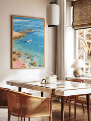 Impressionistic painting of person paddleboarding on clear blue water near rocky coast and pink sand, in a styled room mockup