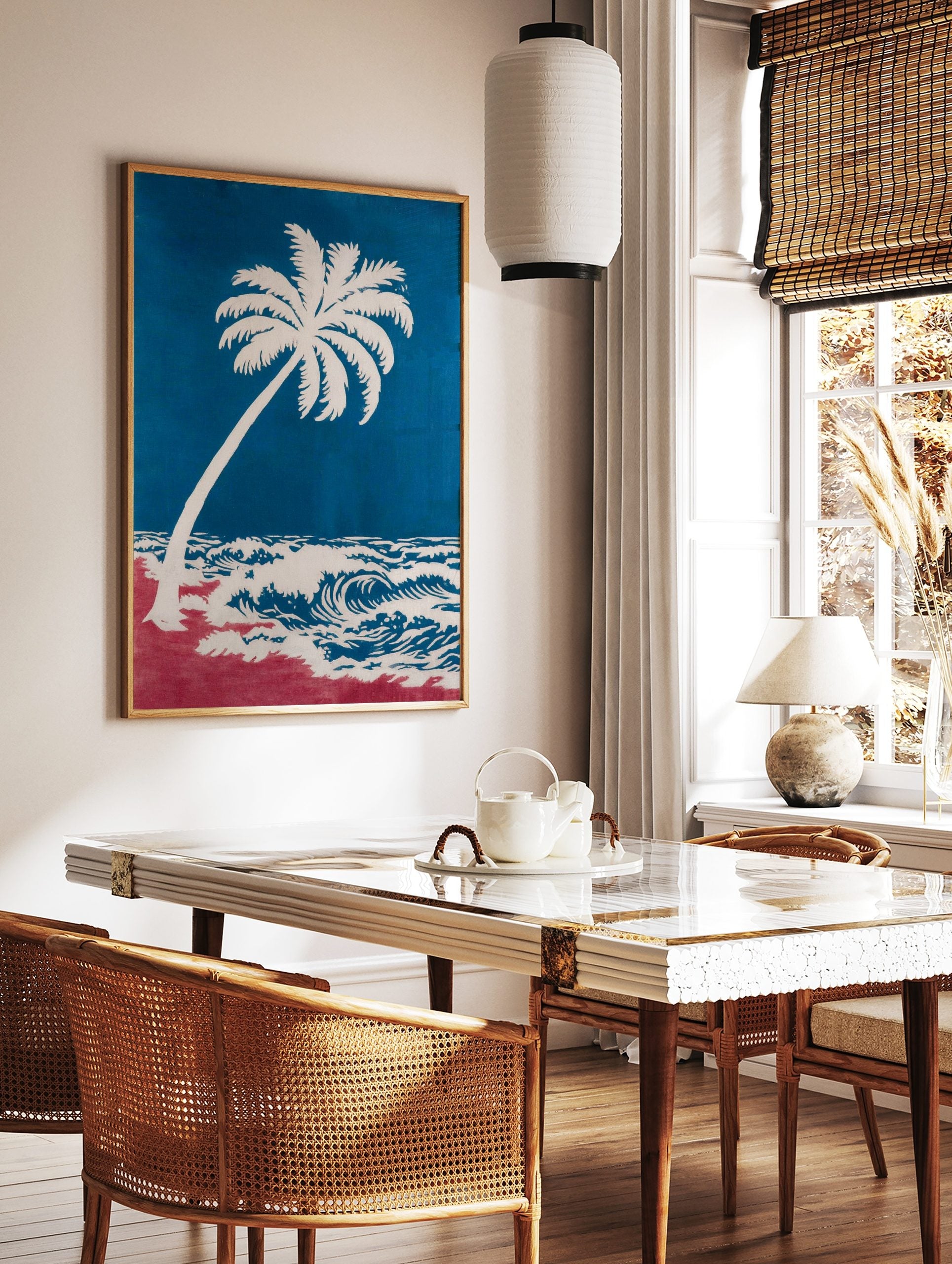 Coastal art print of a white palm tree leaning over blue ocean waves and a red beach, in a styled room mockup