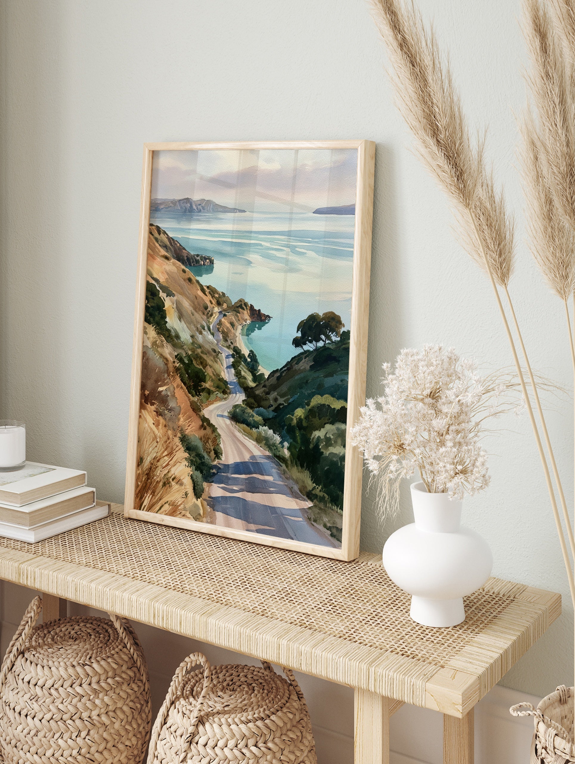 Watercolor-style print of a winding road descending through grassy hills towards a calm, in an alternate framed mockup