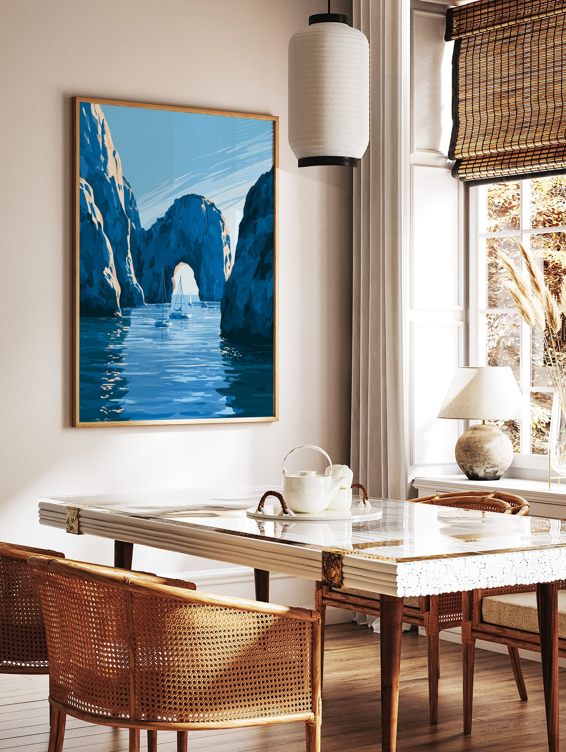 Illustrative coastal wall art print of a natural stone archway over blue water with sailboats, in a styled room mockup