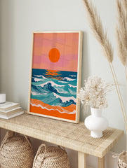 Vibrant coastal sunset art print with large orange sun, blue and teal ocean waves, and orange, in an alternate framed mockup