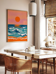 Vibrant coastal sunset art print with large orange sun, blue and teal ocean waves, and orange beach, in a styled room mockup