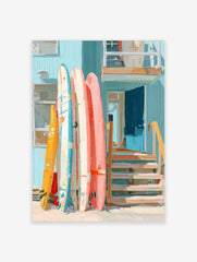 Colourful surfboards leaning against a light blue beach house with an open blue door and wooden stairs