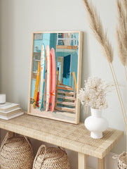 Colourful surfboards leaning against a light blue beach house with an open blue door and, in an alternate framed mockup