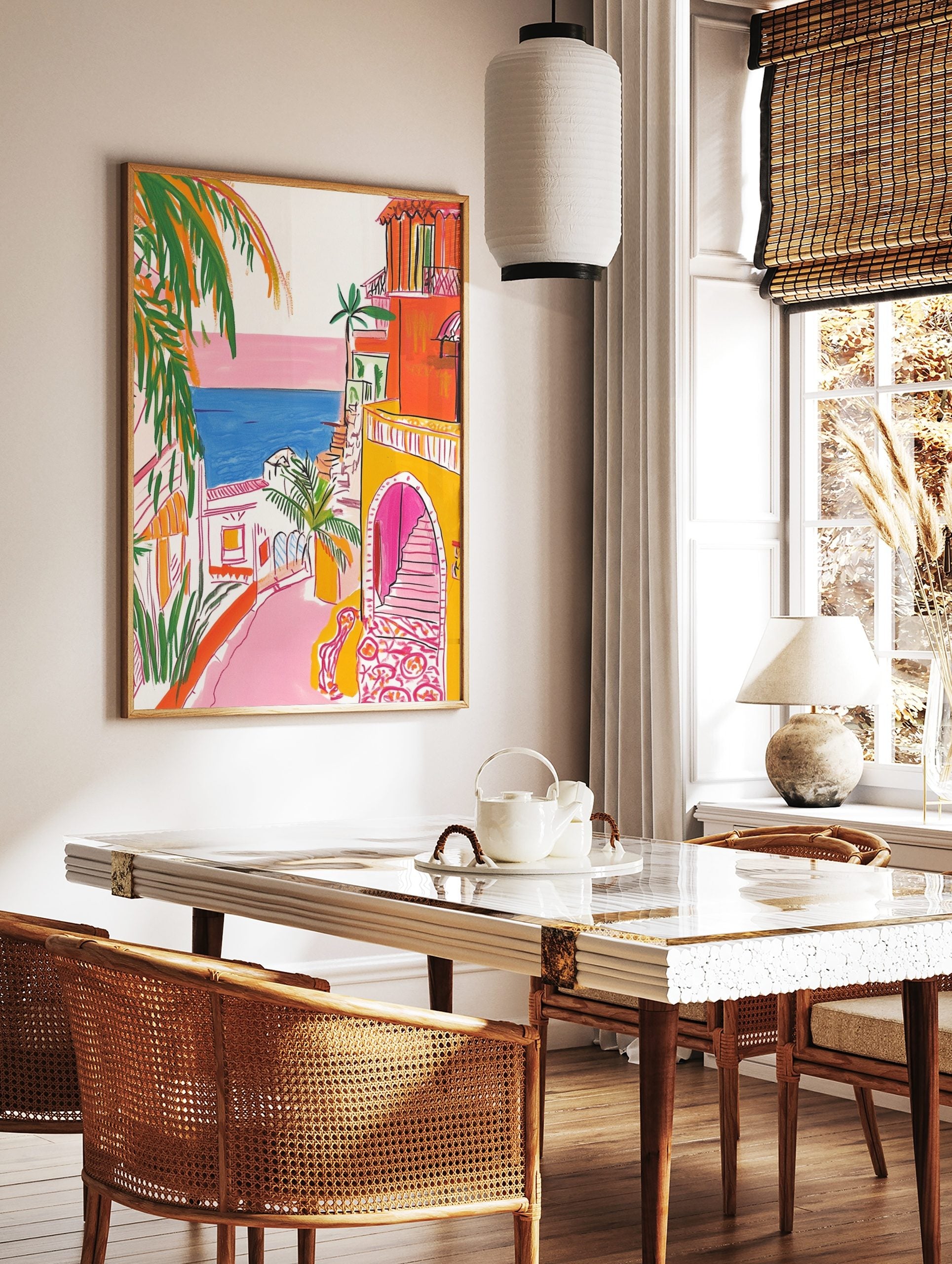 Illustrative coastal town scene with orange buildings, pink street, blue sea, and green palm trees, in a styled room mockup