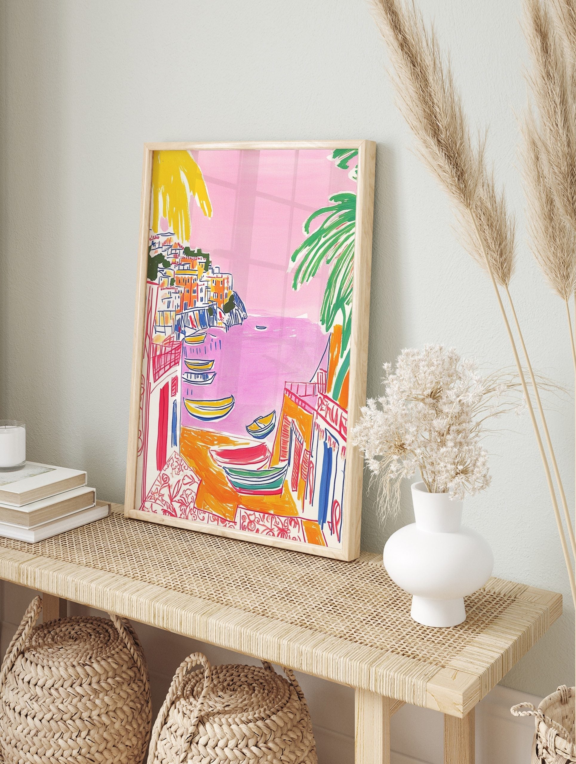 Illustrative print of a colourful coastal town with pink sea, yellow boats, and green palm, in an alternate framed mockup