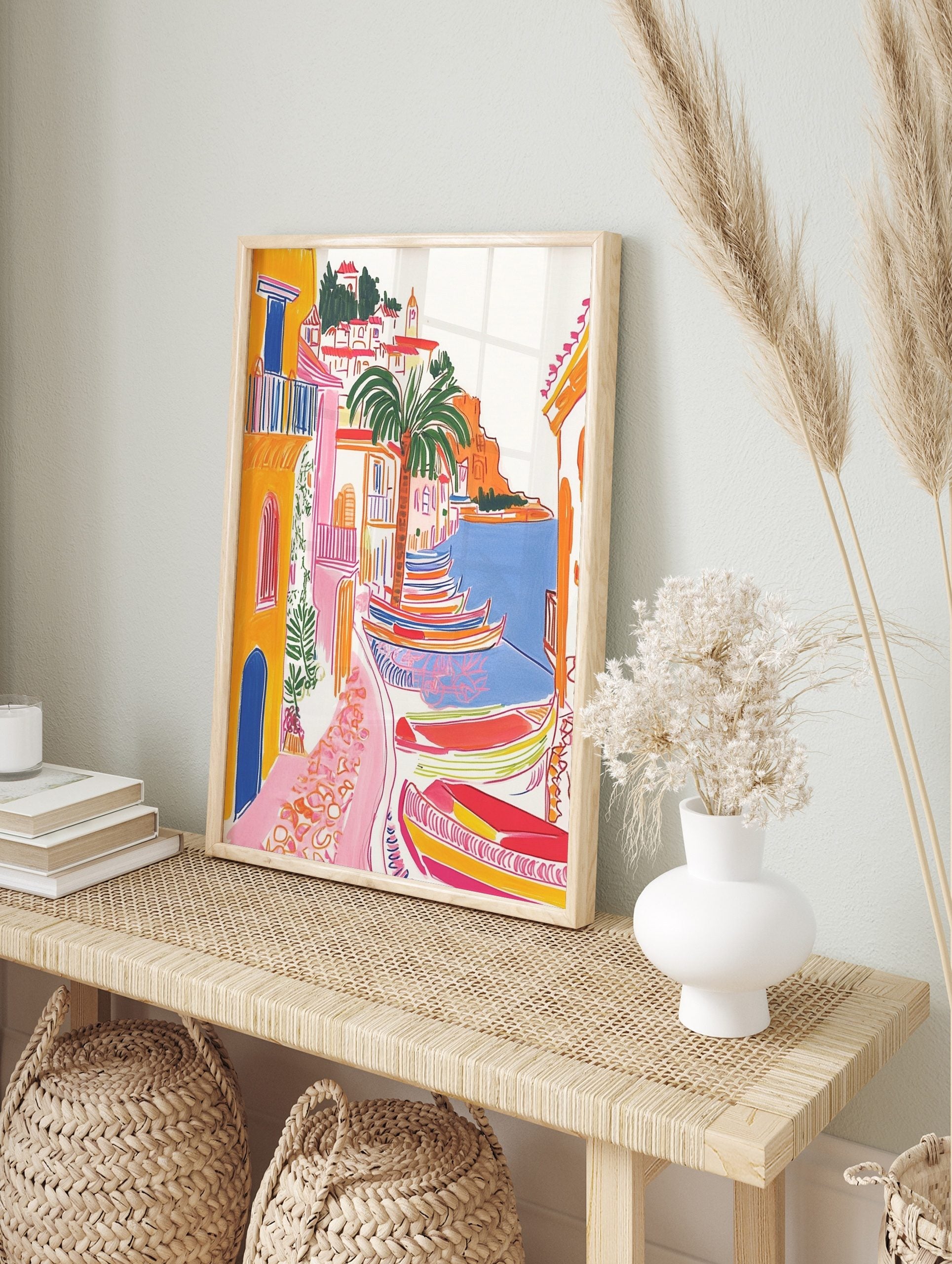 Colourful illustrative coastal village art print with yellow buildings, palm tree, and, in an alternate framed mockup